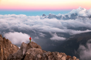 Lonely man stands on top of a mountain ridge, on the background a sea of clouds around the Agner mountain range, Pale di San Martino group, view from Costabella ridge, Dolomites, Italy Lonely man stands on top of a mountain ridge, on the background a sea of clouds around the Agner mountain range, Pale di San Martino group, view from Costabella ridge, Dolomites, Italy